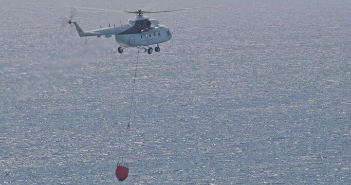 Firefighting Helicopter Scoops Water From Sea. Mi-8 Helicopter For Fighting Forest Fires. Concept Of Help And Rescue In Urgent Situations. Helicopter Bucket To Deliver Water For Aerial Firefighting.