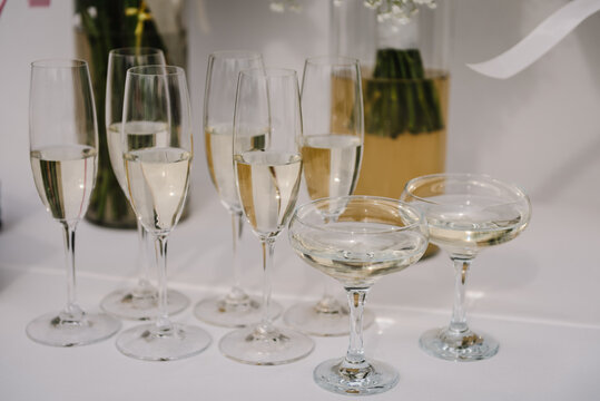 Champagne glasses on table against background of vases with flowers. Catering. Champagne with bubbles on the table. Serving on a wedding party. Drinks serving concept. Cropped shot, selective focus.