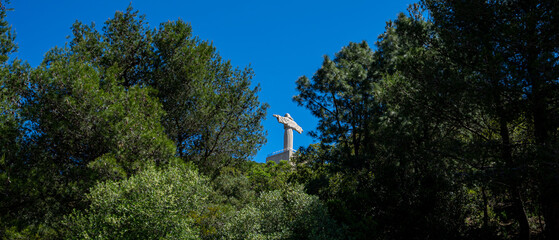 statue of Christ from Almada/Lisbon, Portugal seen through vegetation with strong blue sky.
