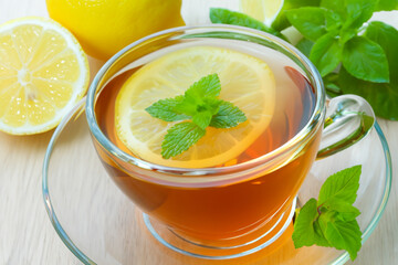 tea composition. on a light wooden table there is a transparent mug with tea and a slice of lemon and a decoration in the form of mint