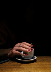 A woman's hand reaching out of the darkness to hold a cup of coffee