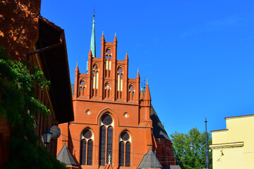The tower of the Catholic church with long windows, decorative elements and crosses, made of red brick. Ancient architecture. Religion and Catholicism. Torun, Poland, August 2023 