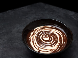 Bowl of hazelnut cream, chocolate paste swirl on black background