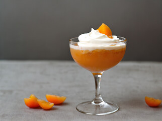 Delicious apricot dessert with whipped cream in glass on grey background