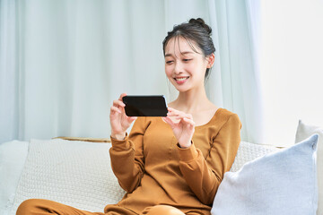 ルームウェアを着てスマートフォンの画面を見る若い女性
