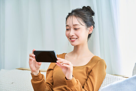 ルームウェアを着てスマートフォンの画面を見る若い女性