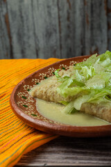 Green Enchiladas with lettuce served in a clay dish on a wooden table.