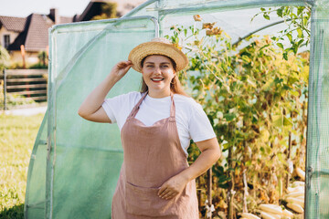 Happy 30s Woman standing in greenhouse. Happy worker growing vegetables and proud of her work in...