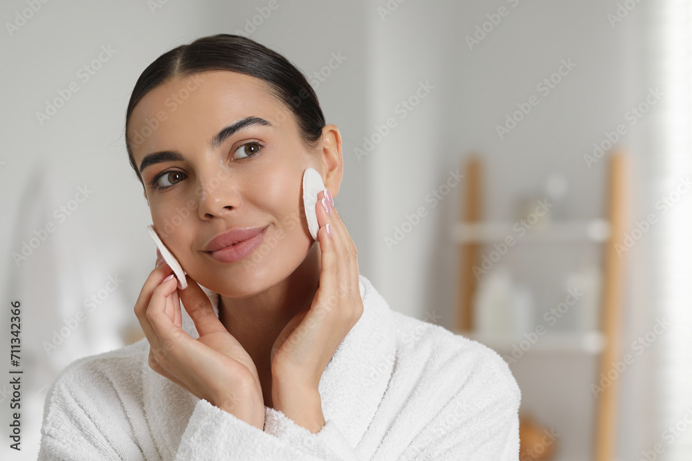 Wall mural Beautiful woman removing makeup with cotton pads in bathroom. Space for text