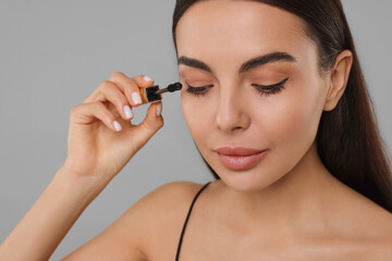 Fototapeta premium Beautiful young woman applying mascara on grey background, closeup