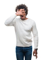 Afro american man over isolated background peeking in shock covering face and eyes with hand, looking through fingers with embarrassed expression.