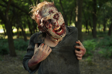 Scary zombie with bloody face outdoors. Halloween monster