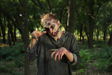 Scary zombie with bloody face outdoors. Halloween monster
