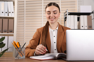 Happy woman taking notes at wooden table in office
