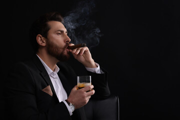 Handsome man in elegant suit with glass of whiskey smoking cigar on black background. Space for text