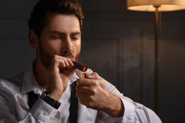 Handsome man lightning cigar at home. Space for text