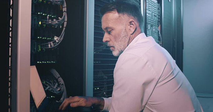 Mature man in server room with laptop, cable for network maintenance or engineer in digital storage for hardware upgrade. Tech support, system administration or technician in datacenter on computer.