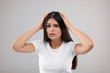 Emotional woman examining her hair and scalp on grey background. Dandruff problem