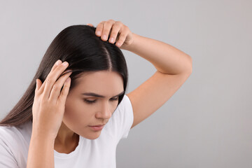 Woman examining her hair and scalp on grey background, closeup. Space for text