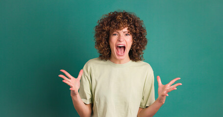 Shocked young woman showing stretched hands with palms on green background