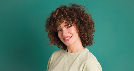 Obraz na płótnie Canvas Smiling standing young curly haired woman on green background