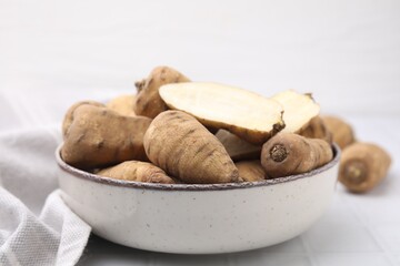 Whole and cut tubers of turnip rooted chervil in bowl on white tiled table, closeup