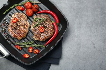 Grill pan with delicious pork steaks, spices and vegetables on grey table, top view. Space for text