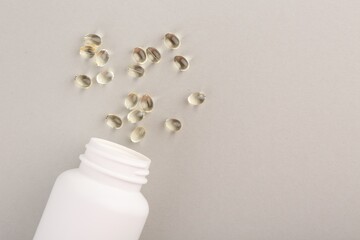 Bottle and vitamin capsules on light grey background, top view. Space for text