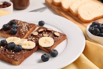 Toasts with tasty nut butter, banana slices, blueberries and hazelnuts on table, closeup