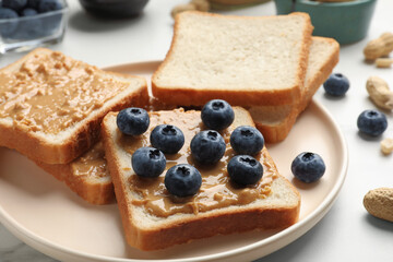 Delicious toasts with peanut butter and blueberries on white table, closeup