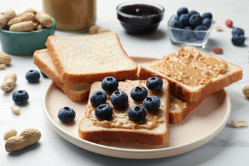 Delicious toasts with peanut butter and blueberries on white marble table, closeup