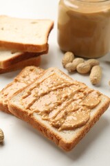 Fototapeta na wymiar Delicious toasts with peanut butter and nuts on white table, closeup