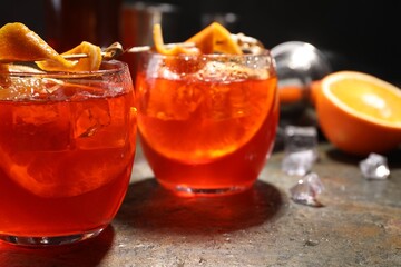 Aperol spritz cocktail, ice cubes and orange slices in glasses on grey textured table, closeup
