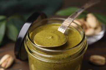 Tasty pistachio cream in jar and spoon on table, closeup