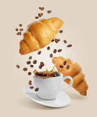 Fresh croissants, aromatic coffee and roasted beans in air on beige background