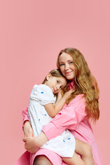 Portrait of happy, beautiful young woman, mother hugging her little daughter against pink studio background. Concept of Mother's Day, International Happiness Day, family, motherhood, childhood