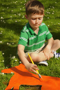 Boy Painting Cardboard Cut Out in Garden
