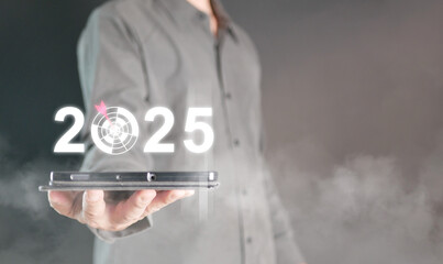 Happy new year 2025. A man holds a tablet with changing year into 2025 with a dartboard in it to set and focus on new goal for the coming new year.
