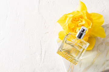 A chic bottle of women's perfume lies on a yellow narcissus, marble podium and a white background Top view. Empty bottle. A copy space.