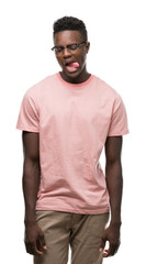 Young african american man wearing pink t-shirt sticking tongue out happy with funny expression. Emotion concept.