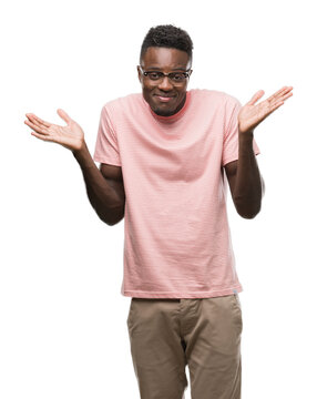 Young african american man wearing pink t-shirt clueless and confused expression with arms and hands raised. Doubt concept.