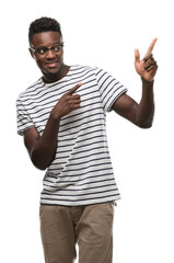 Naklejka premium Young african american man wearing glasses and navy t-shirt smiling and looking at the camera pointing with two hands and fingers to the side.
