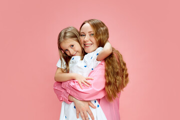 Beauty of motherhood. Young mother embracing her daughter, showing love, support and care against pink studio background. Concept of Mother's Day, International Happiness Day, family, childhood