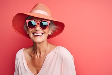 Portrait of happy senior woman in hat and sunglasses on pink background