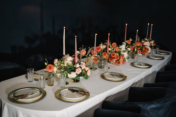 Festive dinner table is served dishes and cutlery and decorated with flowers and greenery, candles. Birthday celebration. Family holidays in modern dining restaurant. Serving, setting table.