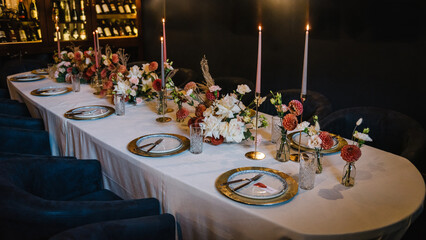Festive dinner table decorated with flowers and greenery, candle. Birthday celebration in restaurant. Serving, setting table. Plate, silverware cutlery, glasses. Wedding set up, dinner table reception