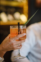 Woman drinking cocktail with slice of orange in a restaurant. Romantic date on Valentine's day. Bride holding fresh juice. Female hand hold cocktail in glass on bar counter at nightclub. Closeup.