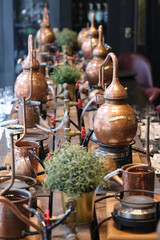 Small copper stills and distilling equipment arranged on a decorated table.