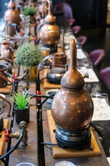 Small copper stills and distilling equipment arranged on a decorated table.