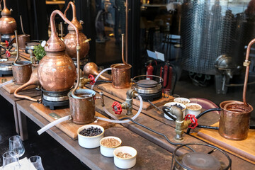 Small copper stills and distilling equipment arranged on a decorated table.